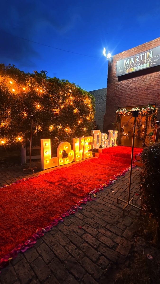 Letras LOVE iluminadas al anochecer sobre la alfombra de pétalos