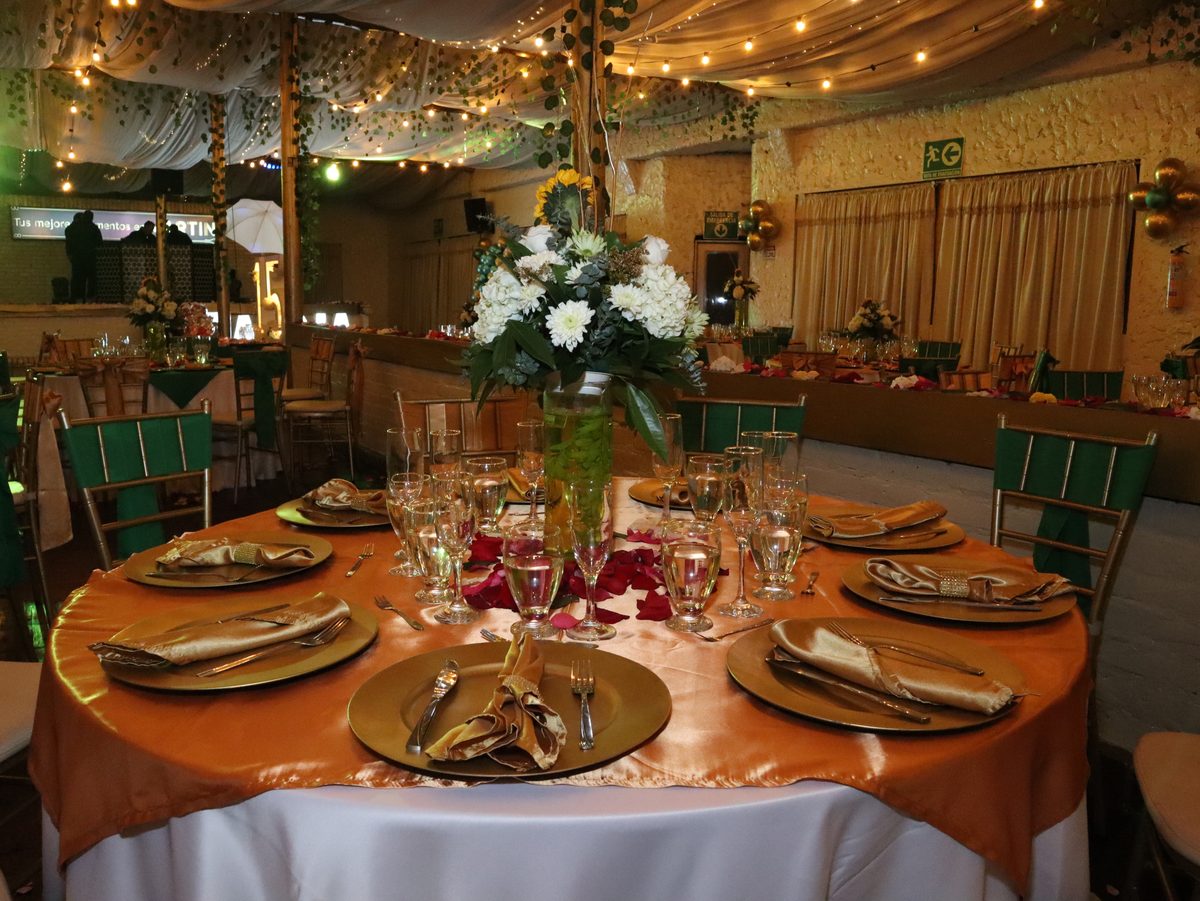 Mesa redonda con mantel dorado y centro floral alto