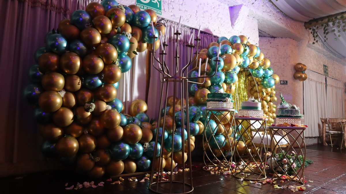 Pared de globos en verde y dorado con la mesa de la torta
